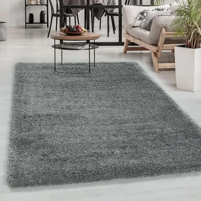 A shaggy gray rug is laid out in a living room setting, with a coffee table and furniture visible in the background.