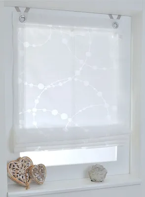 A white Roman blind with a dotted pattern hangs in a window, with decorative hearts and a small statue on the windowsill below.