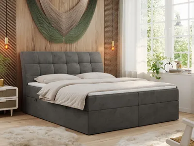 A bedroom scene featuring a large bed with a dark gray upholstered headboard and base, dressed with beige bedding. The room has wooden walls, a large window with sheer curtains, and decorative wall art.