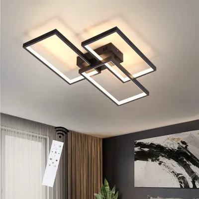 A modern ceiling light fixture with multiple rectangular frames, illuminated and mounted on a ceiling. A remote control is shown in the foreground, with a hint of a window and artwork in the background.