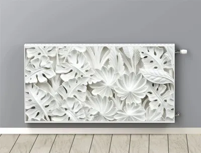 A white radiator cover with a floral leaf design is mounted on a light gray wall above a wooden floor.