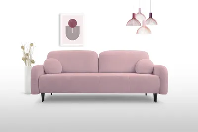A pink sofa is displayed against a white background with a framed picture and a vase of dried flowers on the left, and pendant lights hanging from above.