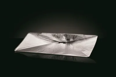 A silver-colored grease tray is shown on a reflective black surface with a dark background.