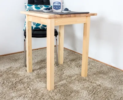A light wood table with a chair behind it, placed on a beige carpet.