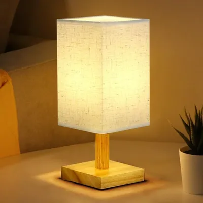 A bedside lamp with a fabric shade and a wooden base is placed on a surface, likely a nightstand or table.