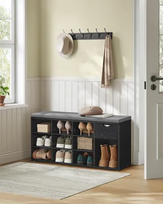 A shoe bench with storage compartments and a drawer, placed in an entryway with a hat and scarf on a wall rack.