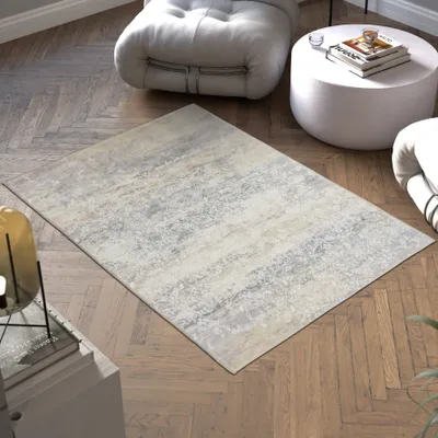 A rug is placed on a wooden floor in a modern living room setting, with furniture like a floor cushion and a round coffee table visible.