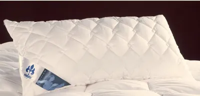 A white quilted pillow on a bed with a dark background.