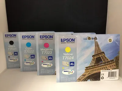 Four Epson ink cartridges are displayed in their packaging, with a picture of the Eiffel Tower on the largest package.