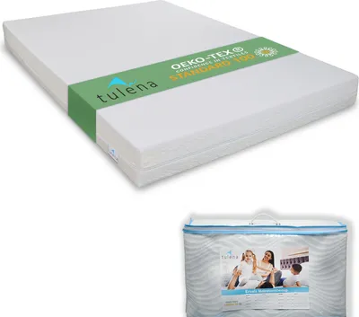 A white mattress topper is shown from a slightly elevated angle, with a green band around it containing brand and certification information. Below it, a clear plastic bag contains a folded duvet or comforter, with a printed image of a family on it.