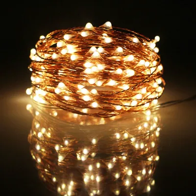 A coiled string of warm white LED lights with a copper wire, reflected on a dark, glossy surface.