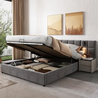 A bedroom scene with a bed that has its storage compartment open, revealing stored items. There are two paintings on the wall and a nightstand next to the bed.
