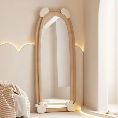 A full-length mirror with a playful bear-ear design, standing in a softly lit room next to a bed.