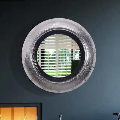 A round mirror with a hammered silver frame hangs on a dark gray wall above a fireplace.