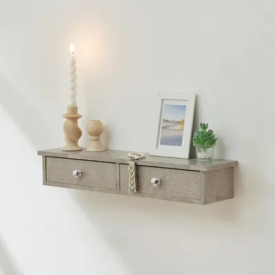 A floating shelf with two drawers mounted on a white wall, decorated with a candle, a picture frame, and a small plant.