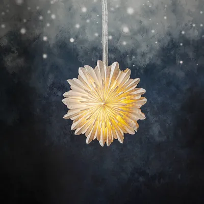 A white paper star lantern hangs against a dark, smoky background with white specks resembling snow.