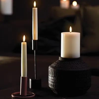 Three LED candles of varying sizes are displayed on a dark surface, with a blurred background suggesting an indoor setting.
