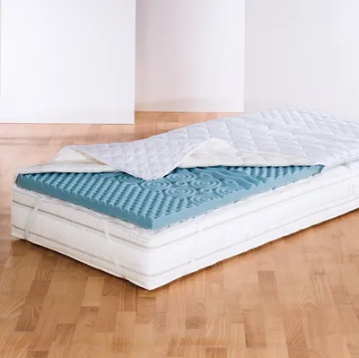 A mattress topper is shown layered on top of a mattress, with a white quilted cover partially covering it.