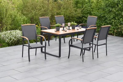 An outdoor dining set with a table and chairs on a patio surrounded by greenery.
