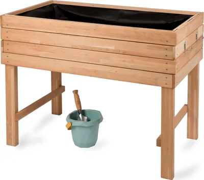 A wooden raised garden bed with a black liner, a small green bucket, and a trowel underneath.