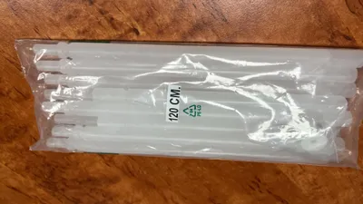 A package of white plastic rods, likely for a curtain or blind, lies on a wooden surface.