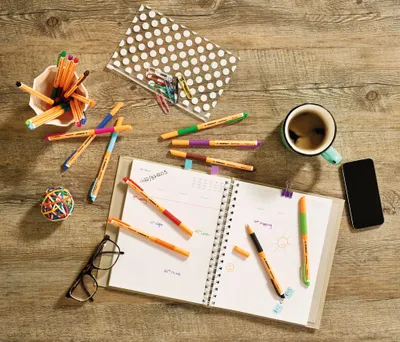 A desk with a planner, pens, coffee, and a smartphone.