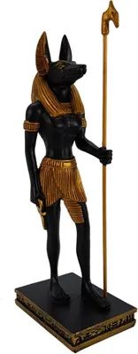 A statue of the Egyptian god Anubis standing on a black and gold base, holding a staff.