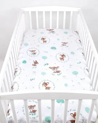 A white crib with a white crib sheet featuring a pattern of deer and trees.
