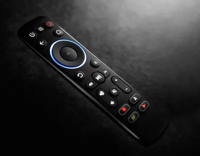 A black remote control is shown on a dark, textured surface with dramatic lighting.
