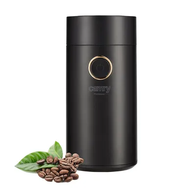 A black coffee grinder with coffee beans and leaves in the foreground, isolated on a white background.
