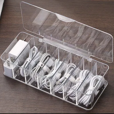 A clear plastic organizer box filled with neatly coiled cables and power adapters, placed on a wooden surface.