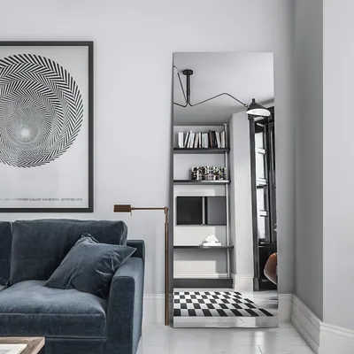 A modern living room with a blue sofa, a large framed poster, and a tall mirror reflecting a bookshelf and a checkered rug.