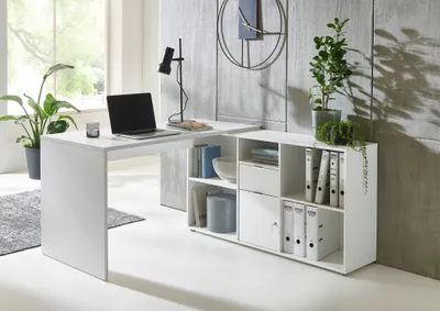 A modern white L-shaped desk with a modular shelving unit attached, set in a bright, contemporary office or home office space.