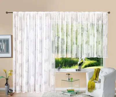 A white lace curtain with a circular pattern is displayed across a window, with a view of greenery outside. A white armchair with a yellow throw is visible to the right.