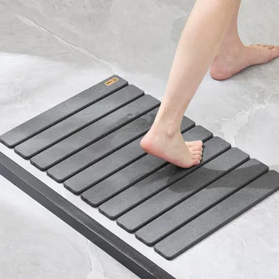 A person's feet stepping onto a grey slatted bath mat.