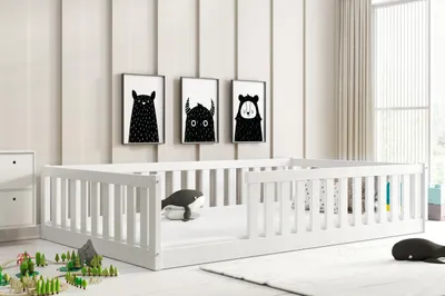 A child's bed with white railings in a room with minimalist decor.