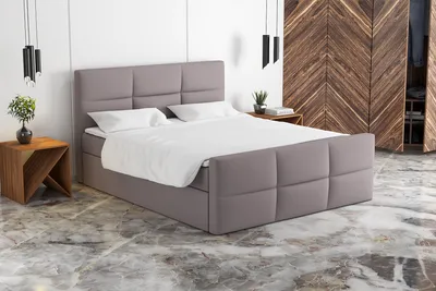 A beige boxspring bed with white bedding is shown in a bedroom setting with a wooden wardrobe in the background.