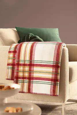 A plaid blanket is draped over the arm of a sofa, with a green pillow behind it.