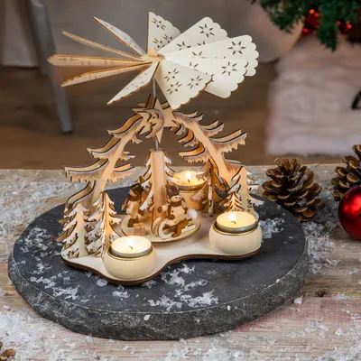 A wooden Christmas pyramid with four tea light holders, set on a dark stone base with artificial snow.