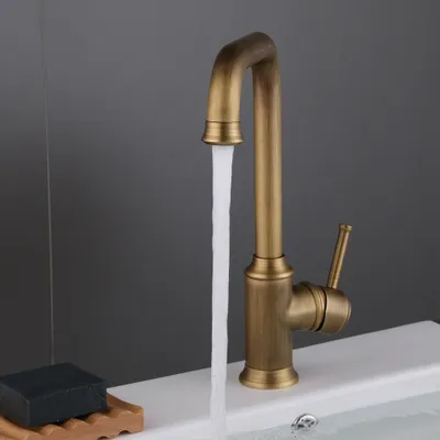 A bronze-colored faucet is shown running water into a white sink. A bar of black soap is on a wooden soap dish to the left.
