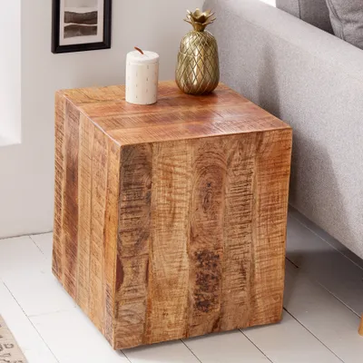 A wooden cube-shaped side table with decorative items on top, next to a sofa.