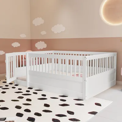A white children's bed with a railing and a gate, set up in a room with cloud decorations on the wall and a dalmatian-print rug on the floor.