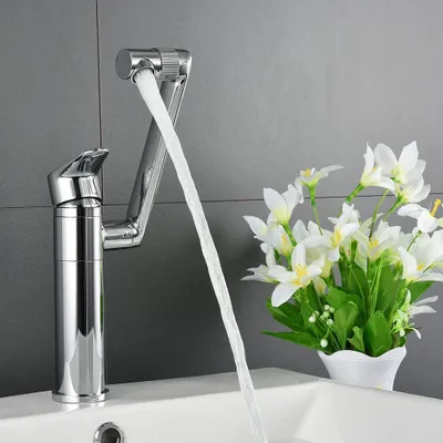 A chrome faucet with water flowing into a white sink, with a vase of white flowers in the background.