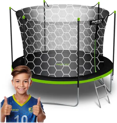 A boy in a soccer uniform gives a thumbs up next to a trampoline.
