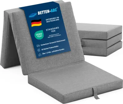 A folded gray mattress is shown in the foreground, with a stack of folded mattresses in the background.