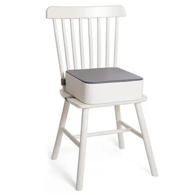 A white wooden chair with a white and gray booster seat for children placed on it.
