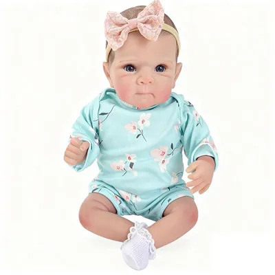 Image de Poupée réaliste : corps en coton de 45 cm, cheveux peints, yeux bleus, cils collés, combinaison longue manche bleue imprimée, chaussettes blanches et bandeau rose pâle avec nœud ajouré.