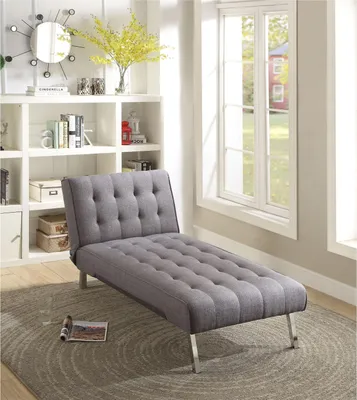 A grey chaise lounge is shown in a well-lit room with a bookshelf and window.