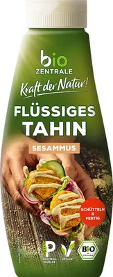 A bottle of liquid tahini with a close-up of falafel sandwiches.
