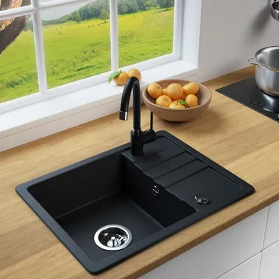A black kitchen sink with a faucet, set on a wooden countertop next to a window with a view of a green landscape. A bowl of oranges is also visible.